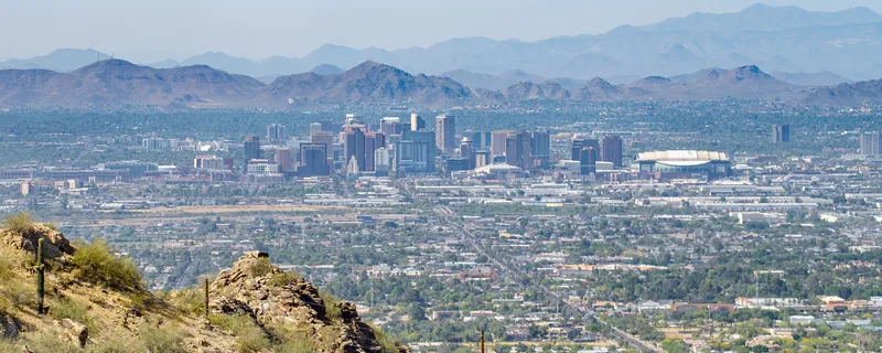 Downtown Phoenix and the surrounding mountains, seen from a desert hillside with saguaro cacti