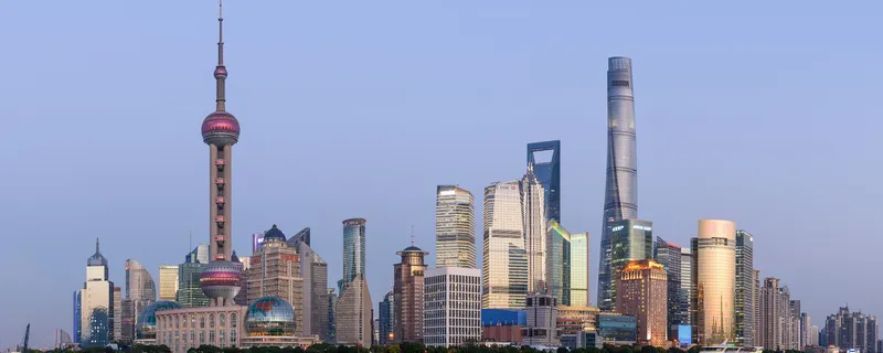 The Pudong skyline across the Huangpu River at dusk, with the Oriental Pearl Tower and Shanghai Tower
